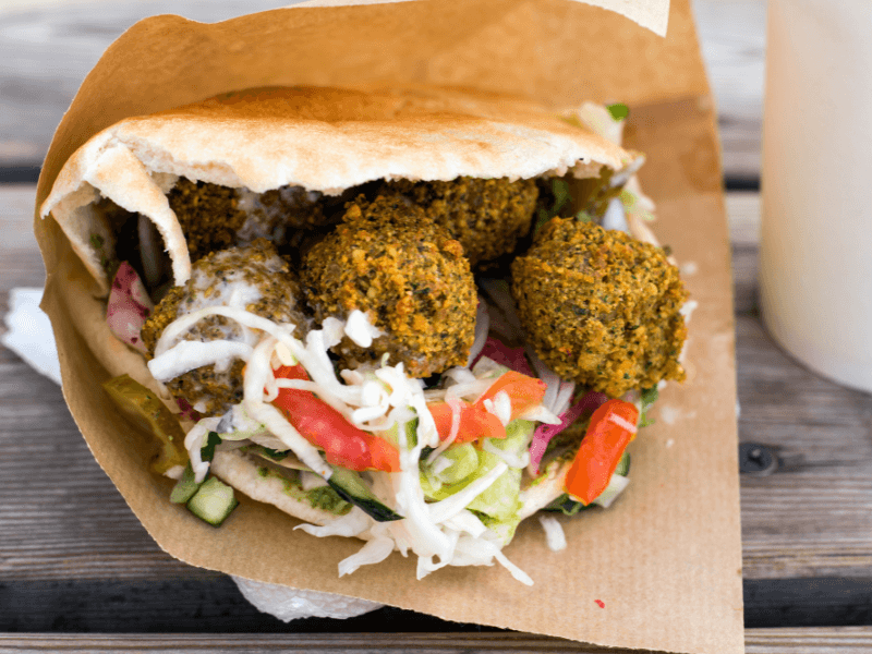 Nahaufnahme eines aufgeschnittenen Fladenbrots gefüllt mit Falafel und Salat.